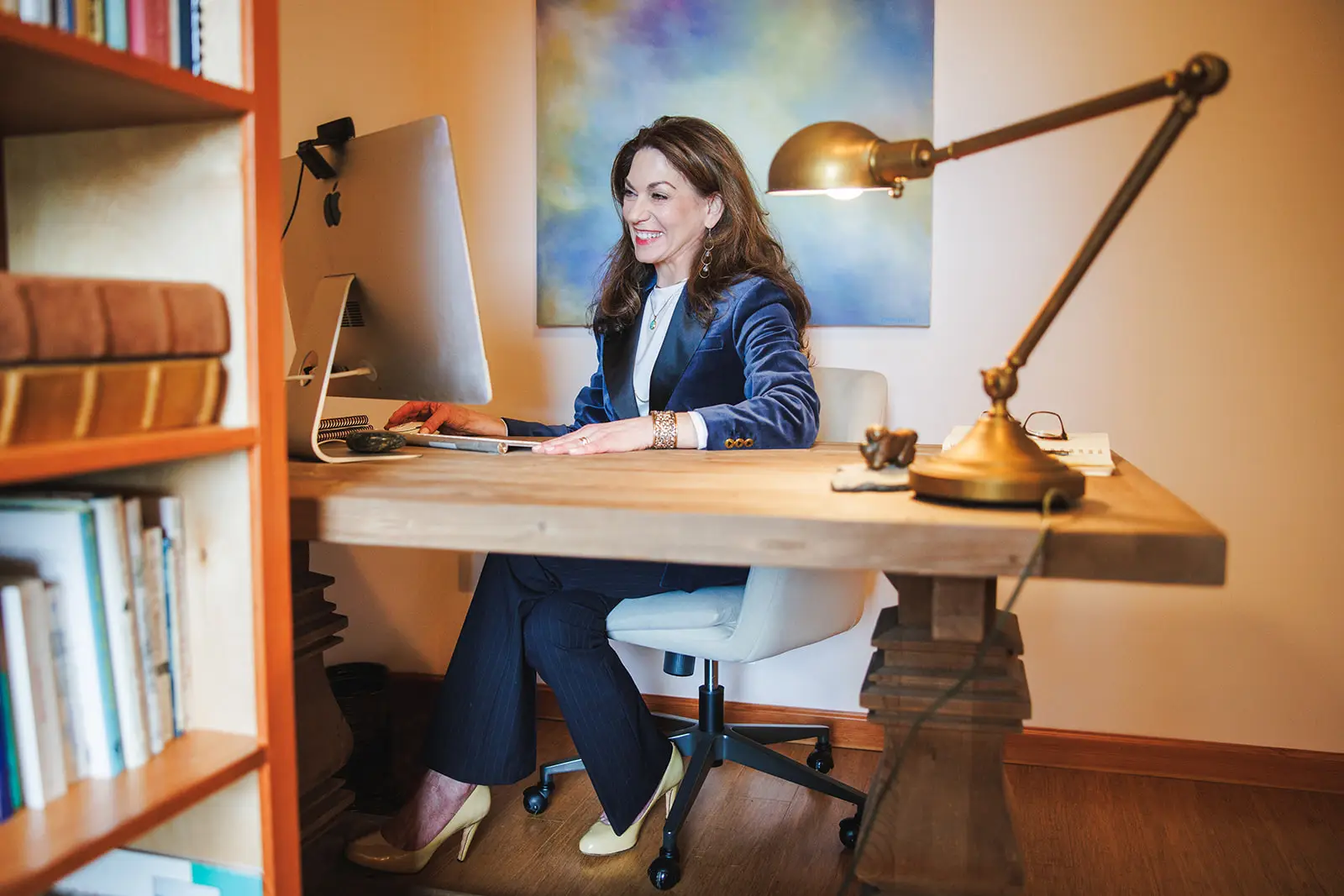 Professional woman working at a desk in a modern home office, smiling at computer, symbolizing productivity, confidence, and work-life balance.